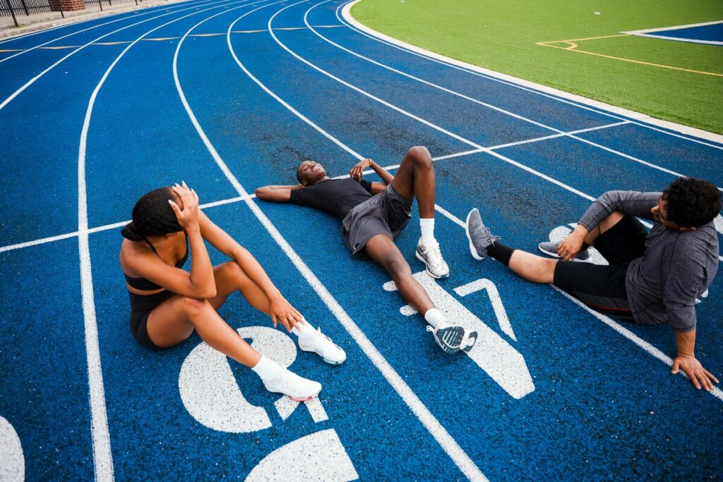 Athletes resting on a blue running track - muscle soreness recovery - fitness friday facts