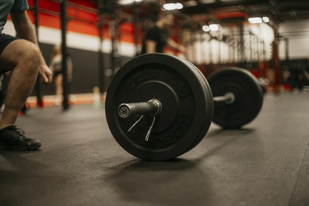 man squatting down next to a barbell in a gym - muscle soreness - fitness friday facts