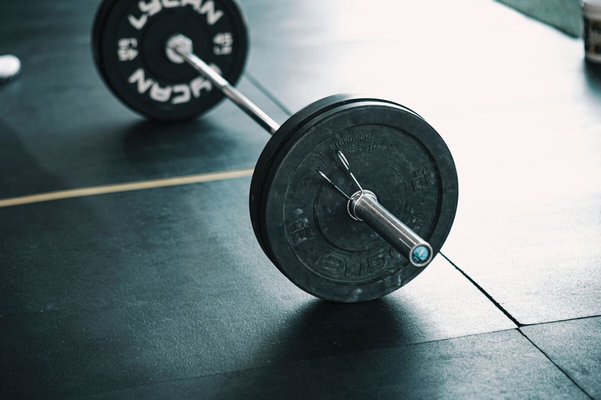Barbell loaded with weight plates resting on gym floor - free weights vs machines - fitness friday facts