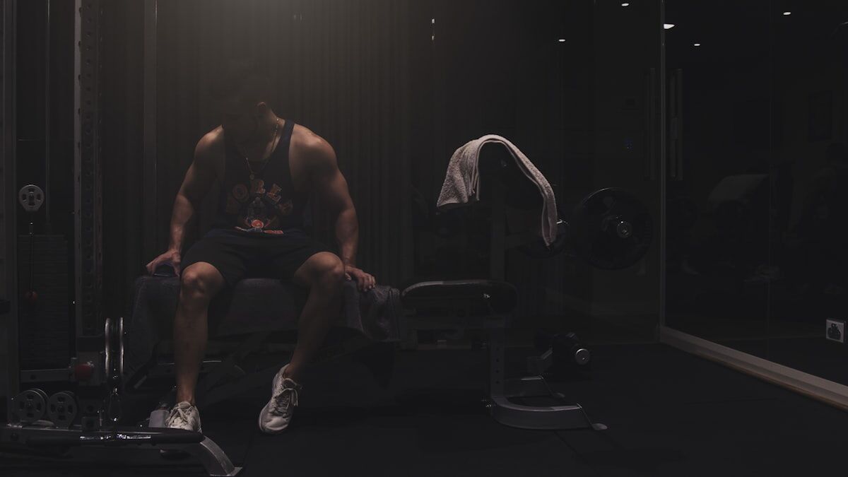 Man sitting on a weight bench focusing between sets - workout rest and recovery - fitness friday facts